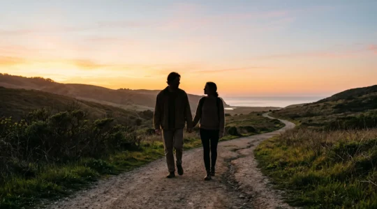 Un couple marchant côte à côte sur un chemin qui passe d'une lumière chaude de coucher de soleil à une lumière douce et stable, symbolisant le passage de l'attirance à une relation durable.